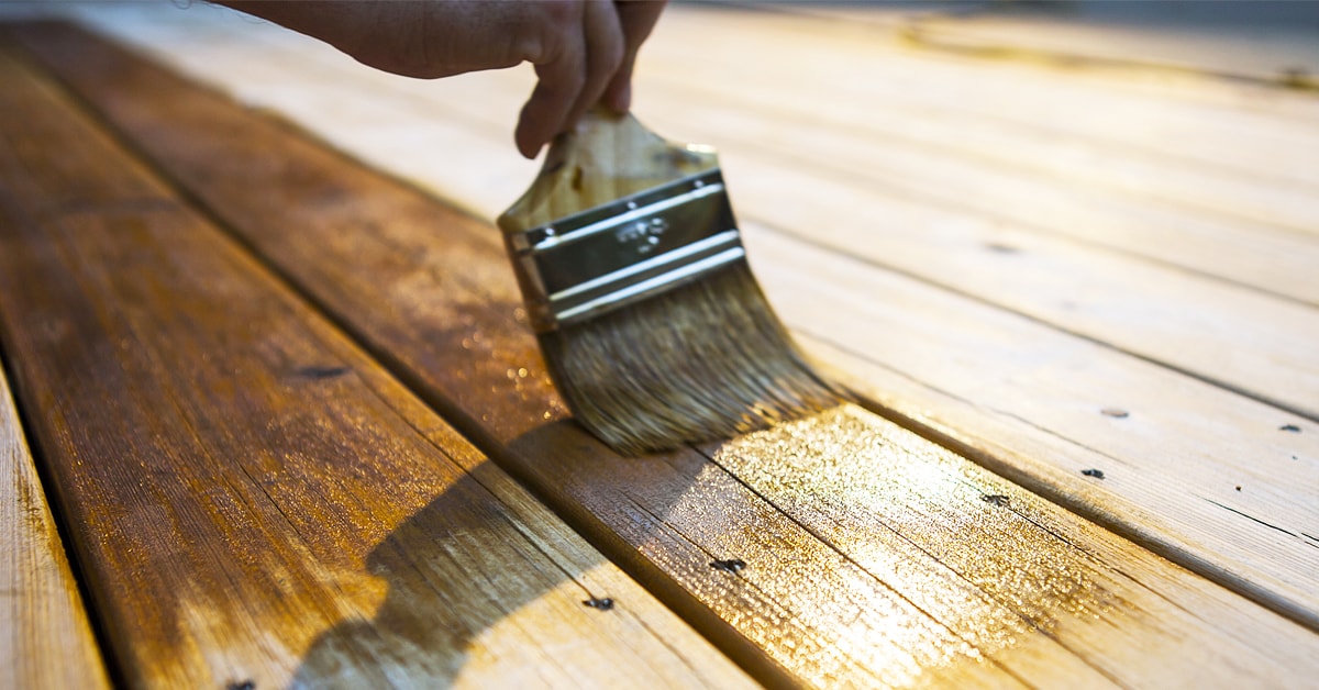 Brush applying stain on a wooden deck